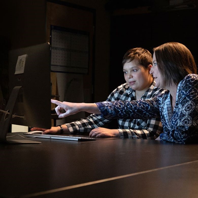 Two people looking at a computer, with one pointing at the screen.