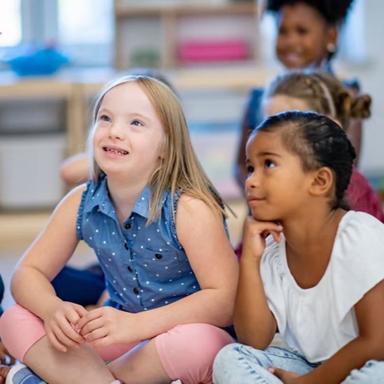 Children crosslegged in classroom, listening.