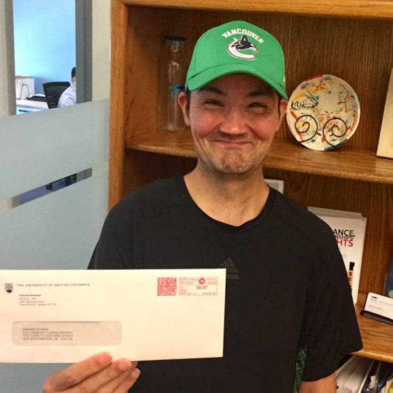 Man smiling and holding official envelope from UBC