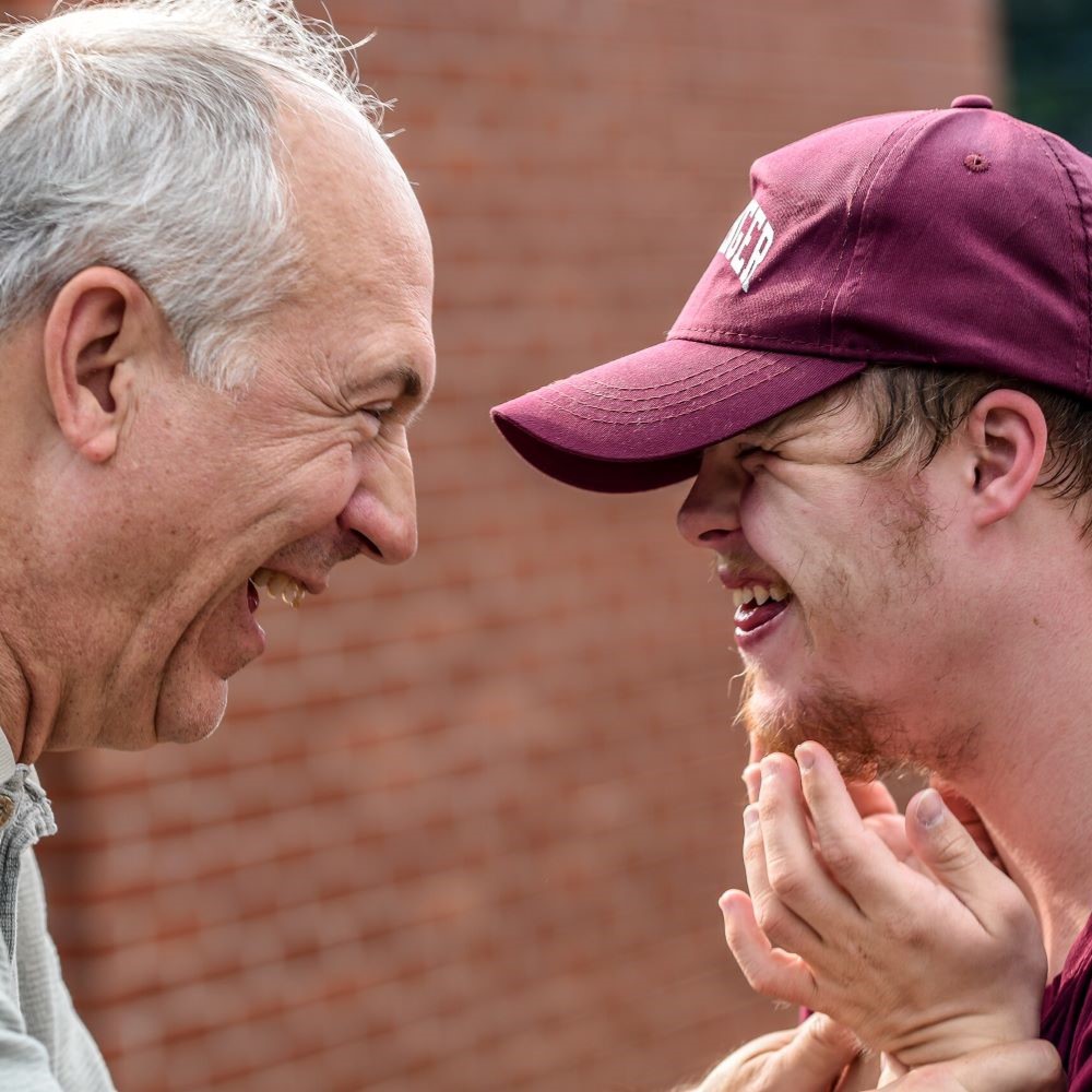 Two men smiling and laughing at each other. One has Down's syndrome.